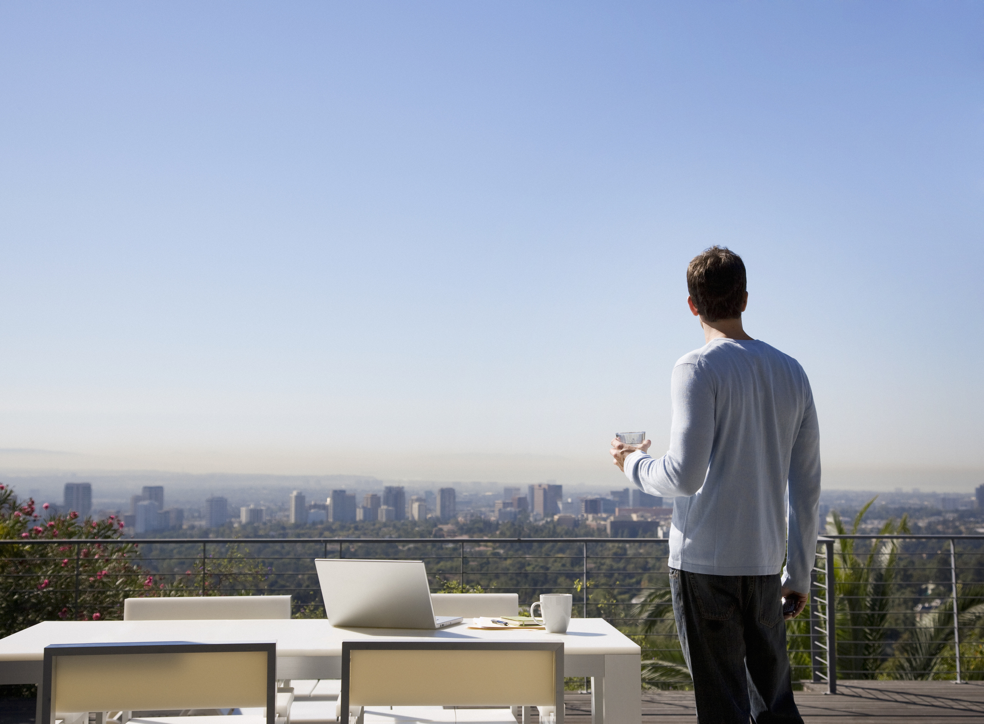 Man using laptop on balcony overlooking city contemplating cross border move